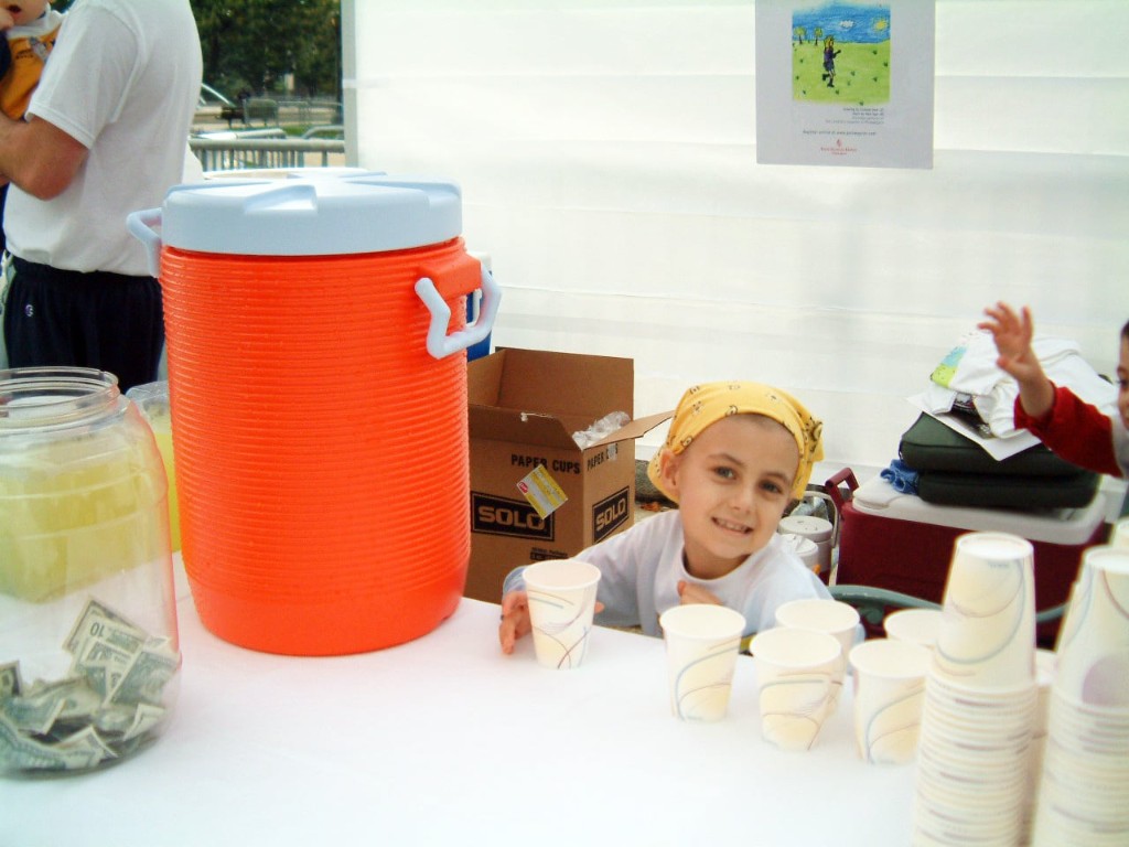 Alexandra Scott at her lemonade stand with cups and a donation jar